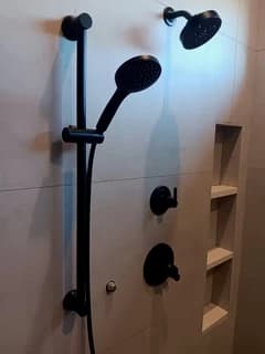 Black showerhead, handheld shower, and controls on a finished wall
